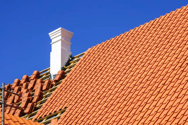 Bright orange tiled roof under construction, white chimney, clear sky. -tile roof replacement