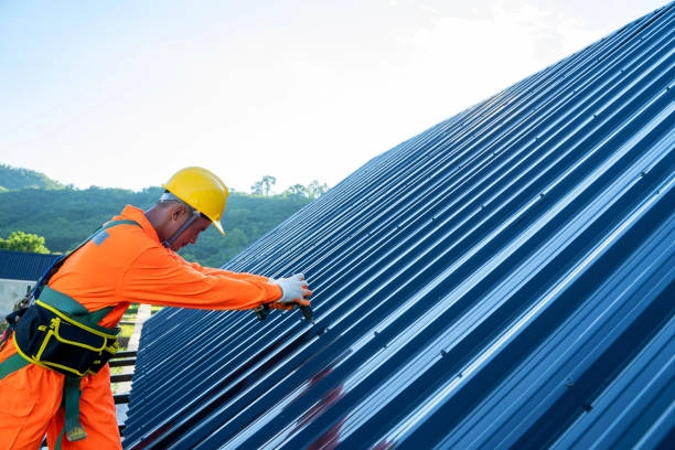 Worker in safety gear installing metal roofing on a building. -commercial roofing contractors