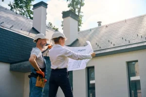 Construction professionals reviewing blueprints outside a modern residential building project. -commercial roof contractors