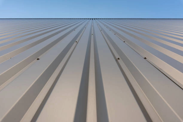 Metal roof with vertical panels and screws under clear blue sky. -commercial roofer contractors