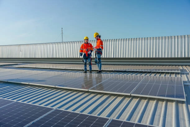 Workers in safety gear inspecting solar panels on a metal roof.-commercial roofer contractors