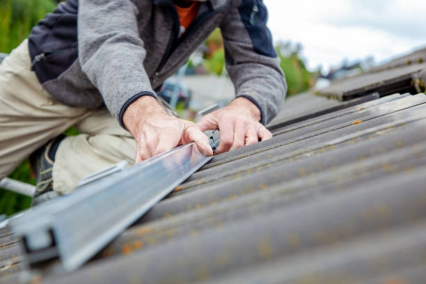 Worker installing metal flashing on an old tiled roof surface. -commercial roofer