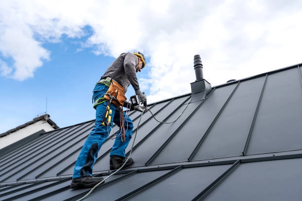 Worker in safety gear repairing a black metal sheet roof. -roof repair phoenix az