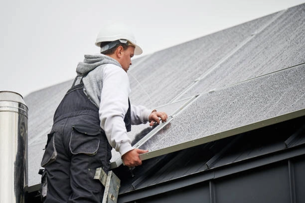 Worker in safety gear installing or repairing rooftop solar panels. -roof repair phoenix az